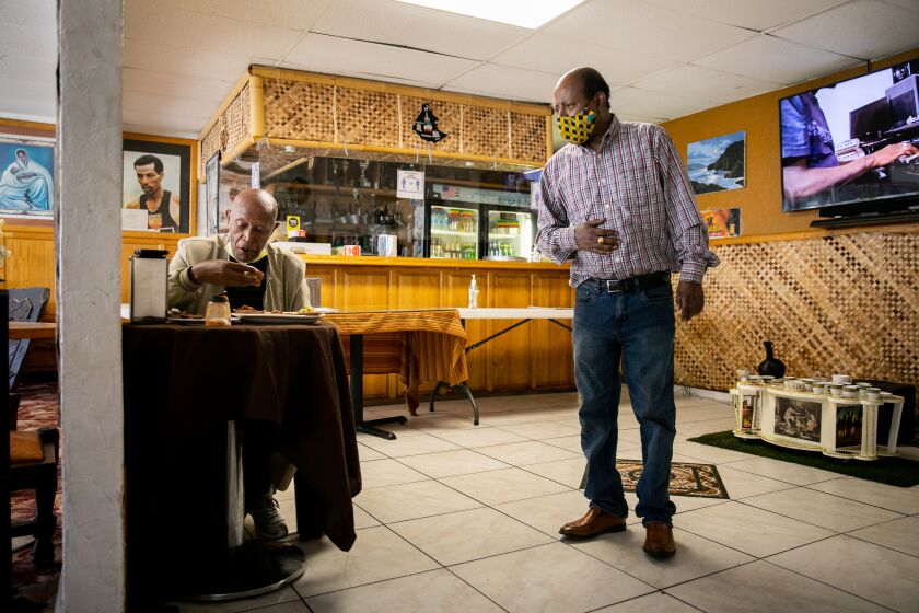 SAN DIEGO, CA - JULY 06: Owner Shimeles Kibret speaks to Mulugeta Gebremariam as he eats in a largely empty dining room at Red Sea, the Ethiopian restaurant, on Monday, July 6, 2020 in San Diego, CA. Kibret is struggling to stay afloat as he works to comply with various governmental orders and other fallout from the coronavirus pandemic. (Sam Hodgson / The San Diego Union-Tribune)