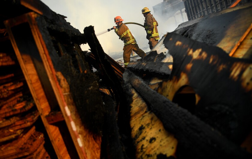 Two firefighters carry a hose past burned wreckage