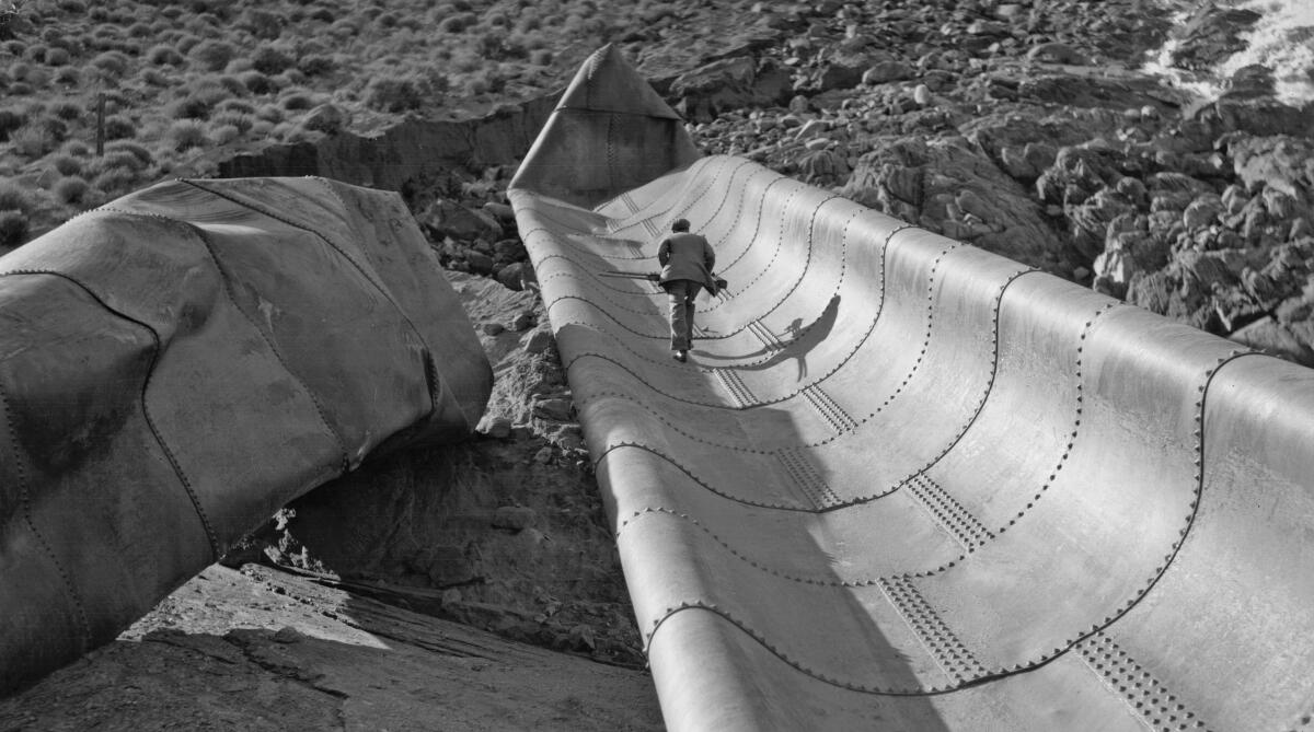 A man walks up a giant piece of collapsed pipe on a hillside.