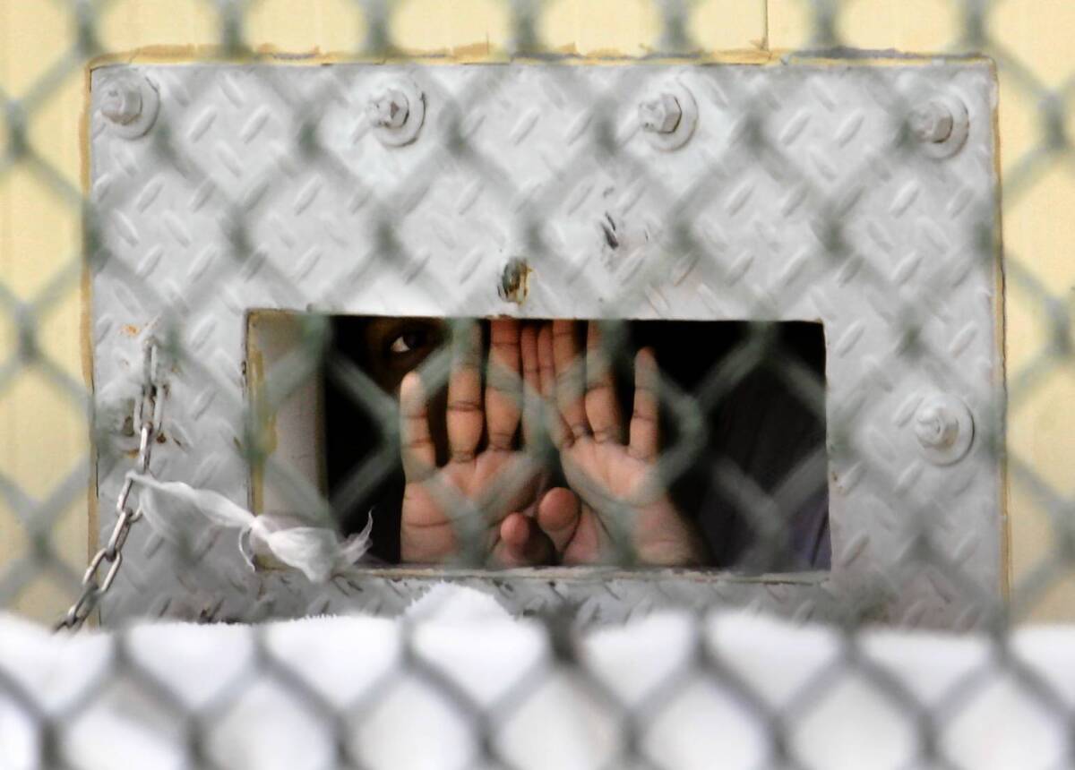 A detainee at the U.S. military's Guantanamo Bay detention center in 2006 shields his face as he peers out through the "bean hole" used to pass food into detainee cells. About 100 prisoners at Guantanamo are on hunger strikes, with some being force-fed through tubes.