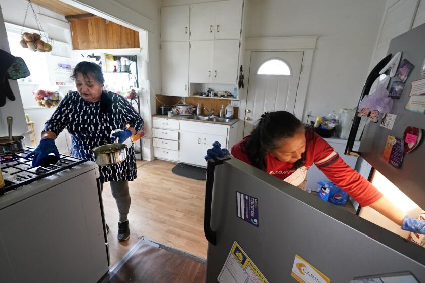 Olga García, a la izquierda, coloca una sartén en una estufa y su hermana Francis saca cosas del refrigerador mientras preparan una comida familiar en su casa en Sedro-Woooley, Washington, el miércoles 4 de noviembre de 2020. (AP Foto/Elaine Thompson)