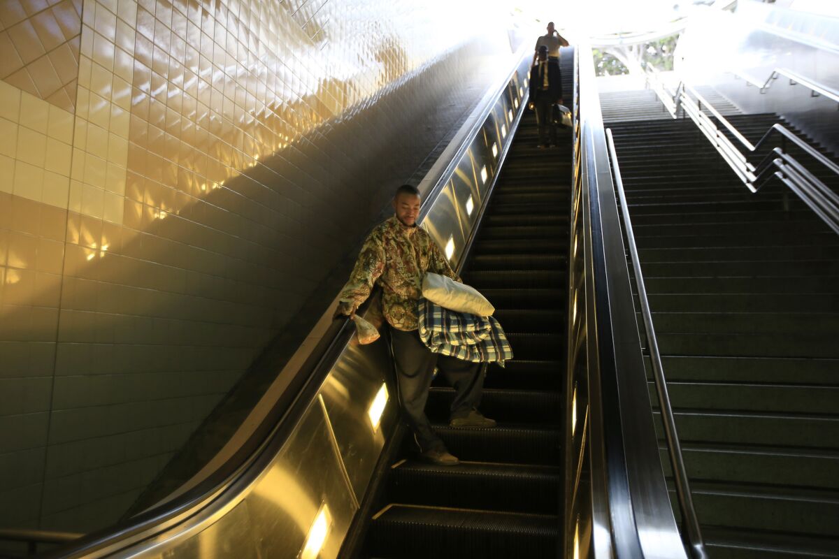 Zackery Joe, 26, carries his pillow and blanket down the escalator into the Civic Center/Grand Park Subway Station.