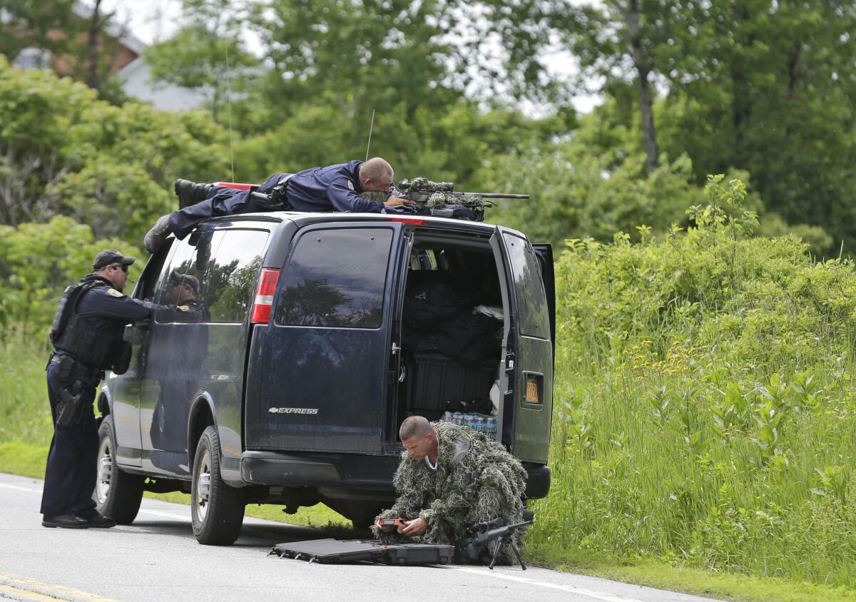A law enforcement agent looks through a sniper scope while another in camouflage assembles a weapon during a search for two escaped killers in Boquet, N.Y., on Tuesday.