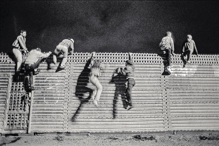 JUNE 18, 1992. SAN YSIDRO, CA. "Too Hungry to Knock" A pair of young men free fall down the north side of the U.S/Mexico border fence. A smuggler straddling the locked door on the left keeps a lookout for U.S. Border Patrol. Hours before this I listened to voices through the steel barrier offering stories of poverty and the desire for a better life. But when the smuggler whistled, the barrier thundered loud from climbing feet and banging knees. 6 men sprinted past me in pursuit of their future. (Photograph by Don Bartletti / Los Angeles Times)
