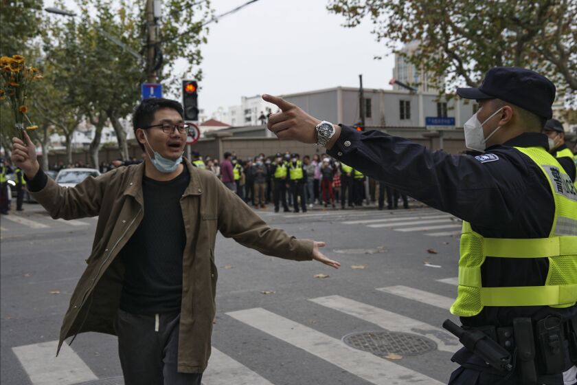 FILE - A protester holding flowers is confronted by a policeman during a protest on a street in Shanghai, China on Nov. 27, 2022. What started as an unplanned vigil last weekend in Shanghai by fewer than a dozen people grew hours later into a rowdy crowd of hundreds. The protesters expressed anger over China's harsh COVID-19 policies that they believed played a role in the deadly fire on Nov. 24 in a city in the far west. (AP Photo, File)