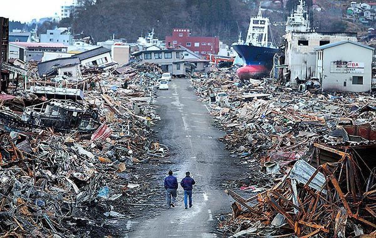 Government officials walk down a recently cleared roadway where the earthquake-spawned tsunami caused a massive fuel spill and fire in Kesennuma, Japan.