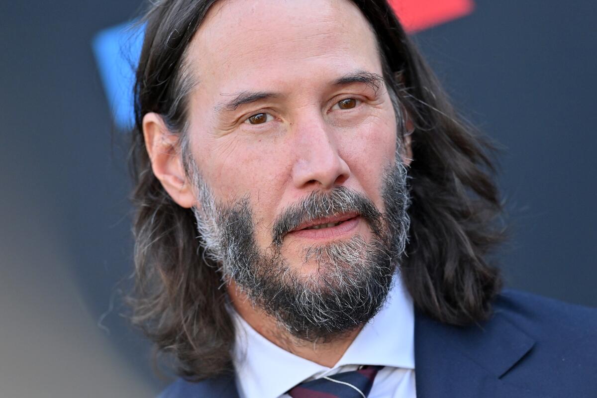 A head-and-shoulders portrait of Keanu Reeves, dressed in a suit and tie