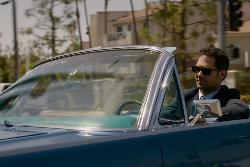 A man in a suit and sunglasses driving a blue convertible in Los Angeles