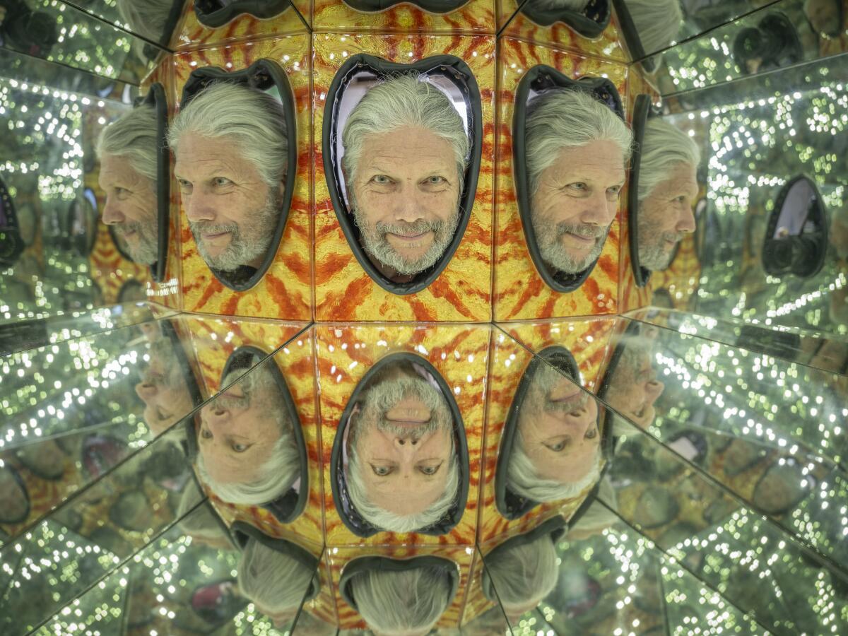 A man with white hair and beard pokes his head through a colorful facade, an image that mirrors multiply to trippy effect. 