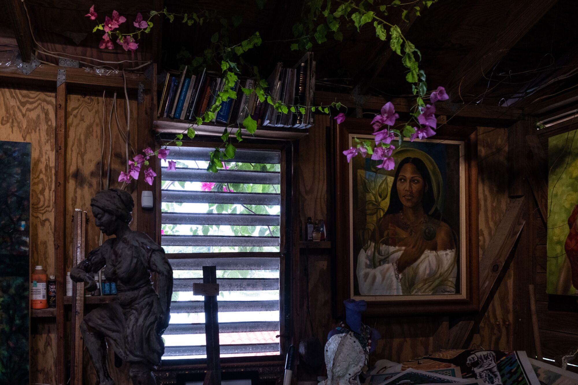 Bougainvillea drapes over a window next to a painting and a sculpture
