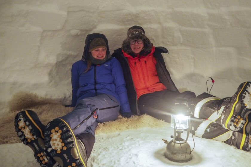 In this handout photo provided by British Antarctic Survey, field guide Sasha Doyle, left, and meteorological observer Jack Farr, right, sit in an igloo in Trident area, Adelaide island, in Antarctica in October 2019. Antarctica remains the only continent without COVID-19 and now in Sept. 2020, as nearly 1,000 scientists and others who wintered over on the ice are seeing the sun for the first time in months, a global effort wants to make sure incoming colleagues don't bring the virus with them. (Robert Taylor/British Antarctic Survey via AP)