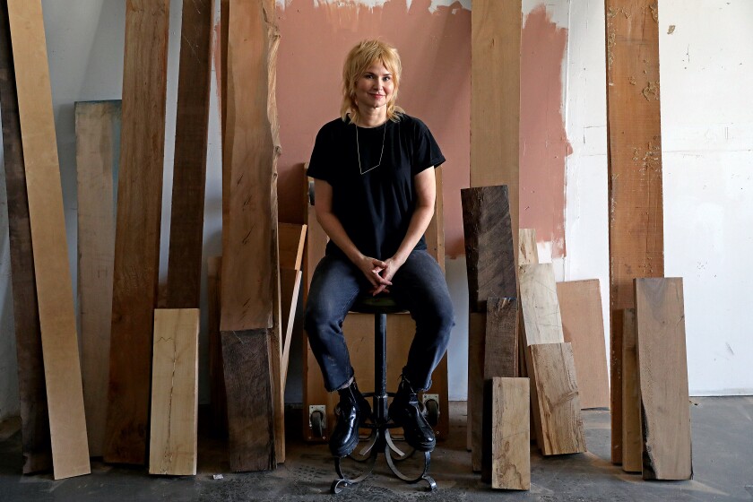 A woman in a black T-shirt and jeans sits amid a bunch of wooden slats.