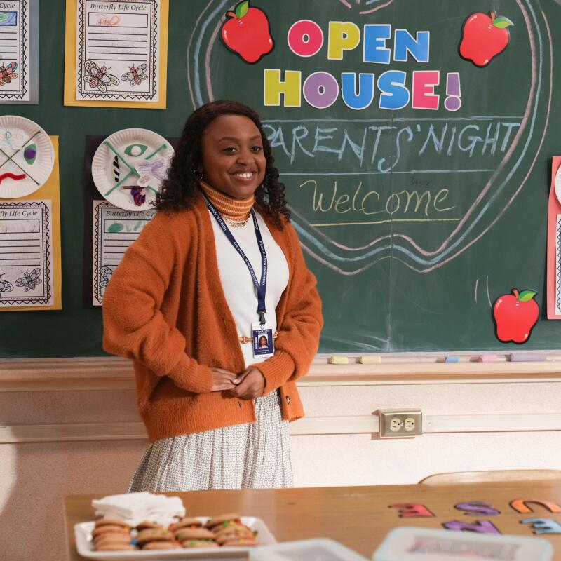 A teacher stands in front of a chalkboard that reads "Open House! Parents' Night. Welcome."
