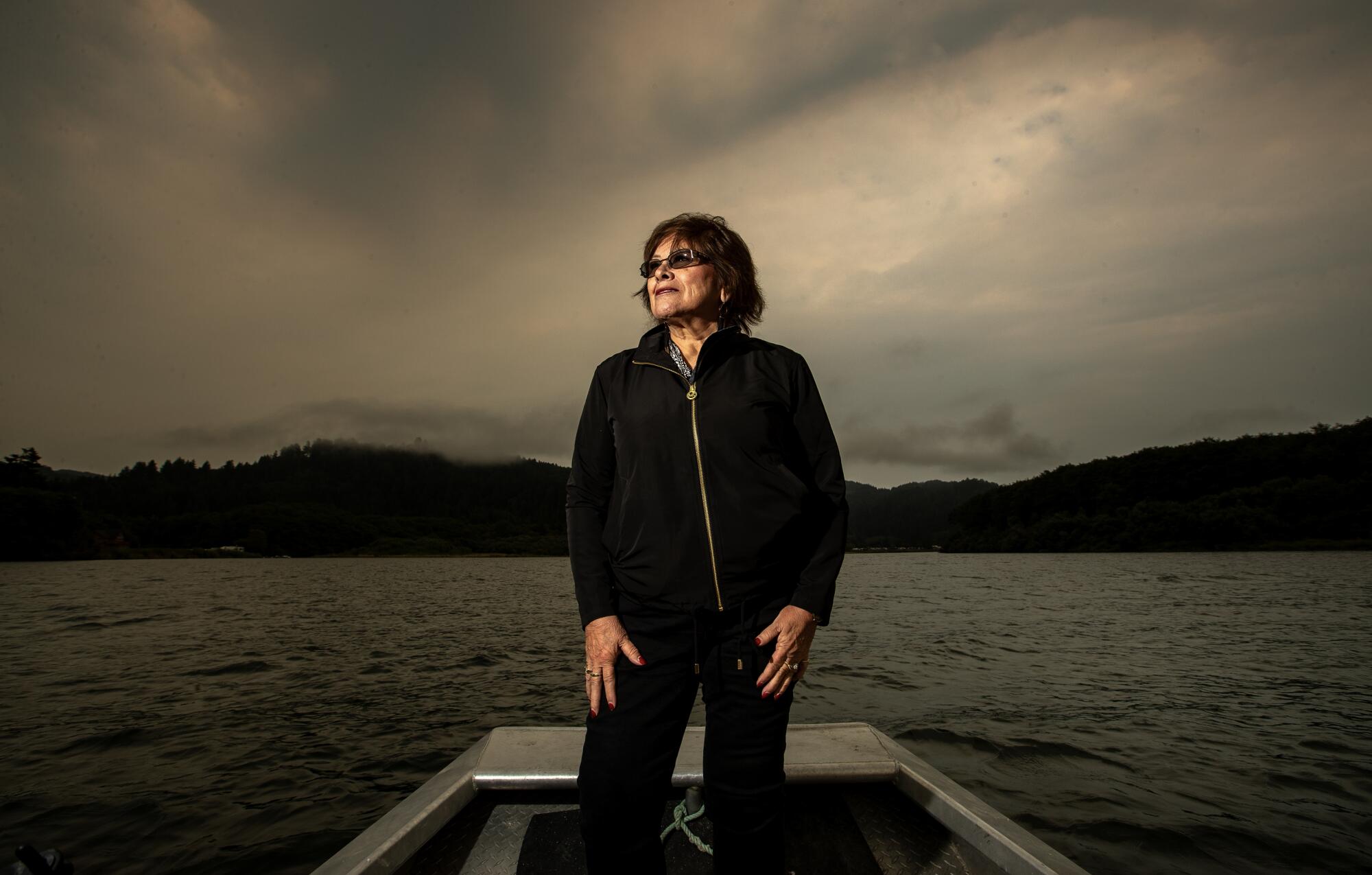 A woman stands in a boat against a dark sky.