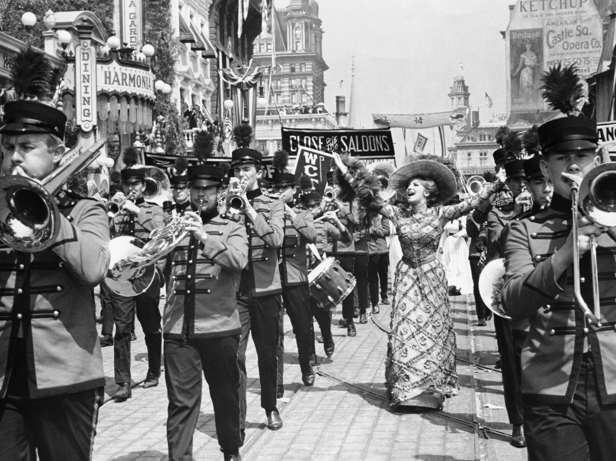 In a black-and-white film still, Barbra Streisand marches with a band in the movie "Hello, Dolly!"