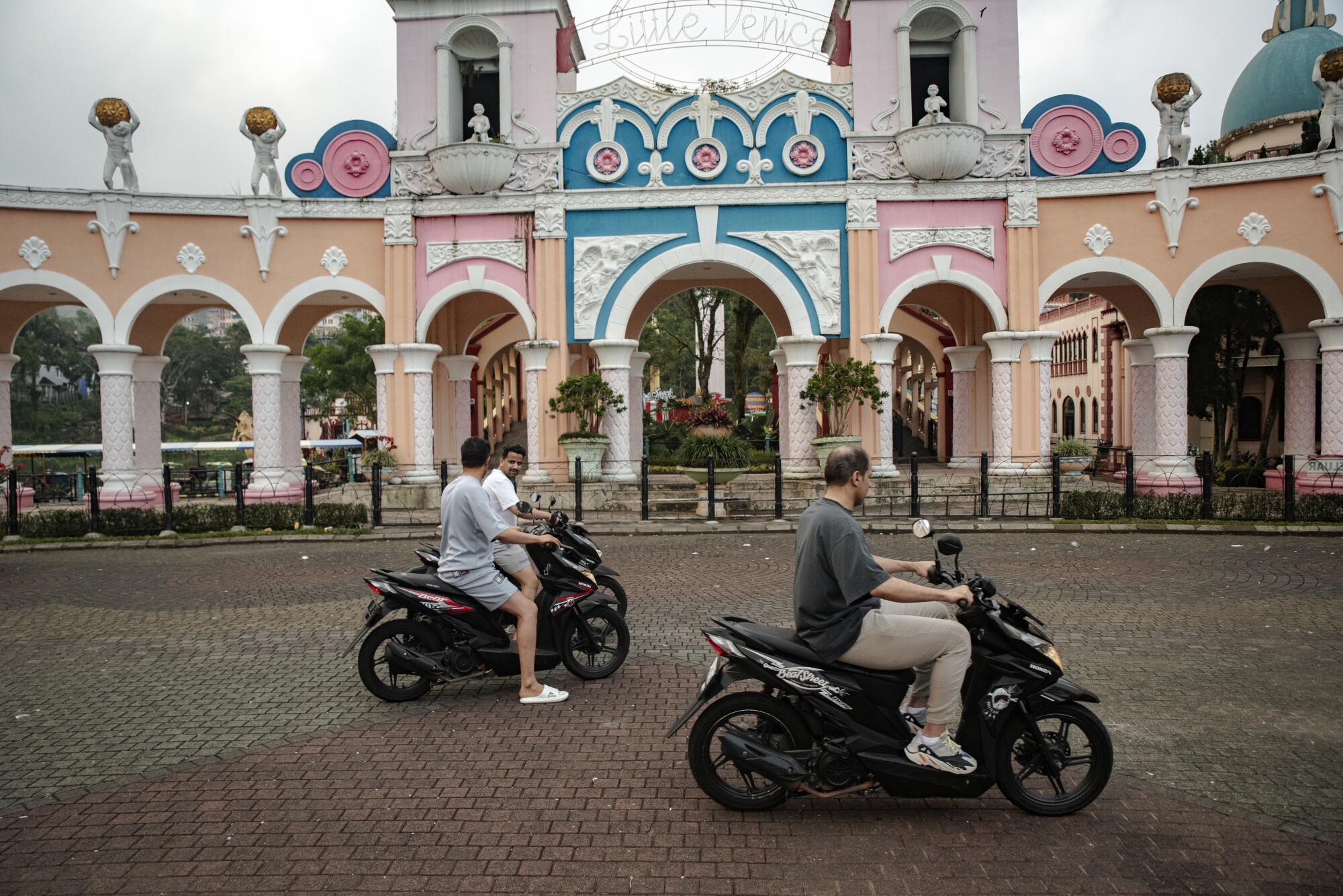 Three travelers ride motorbikes outside of a tourist attraction modeled after Venice in Italy. 