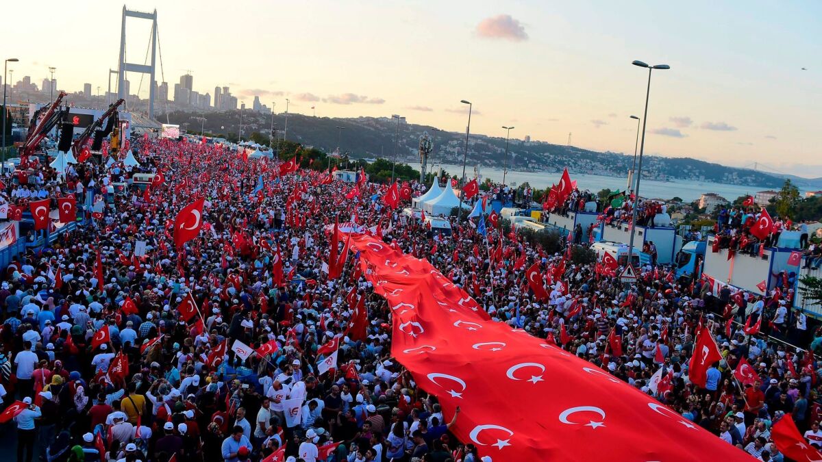 People stand under a collection of Turkish national flags as they gather on the recently renamed July 15 Martyrs Bridge over the Bosporus in Istanbul.