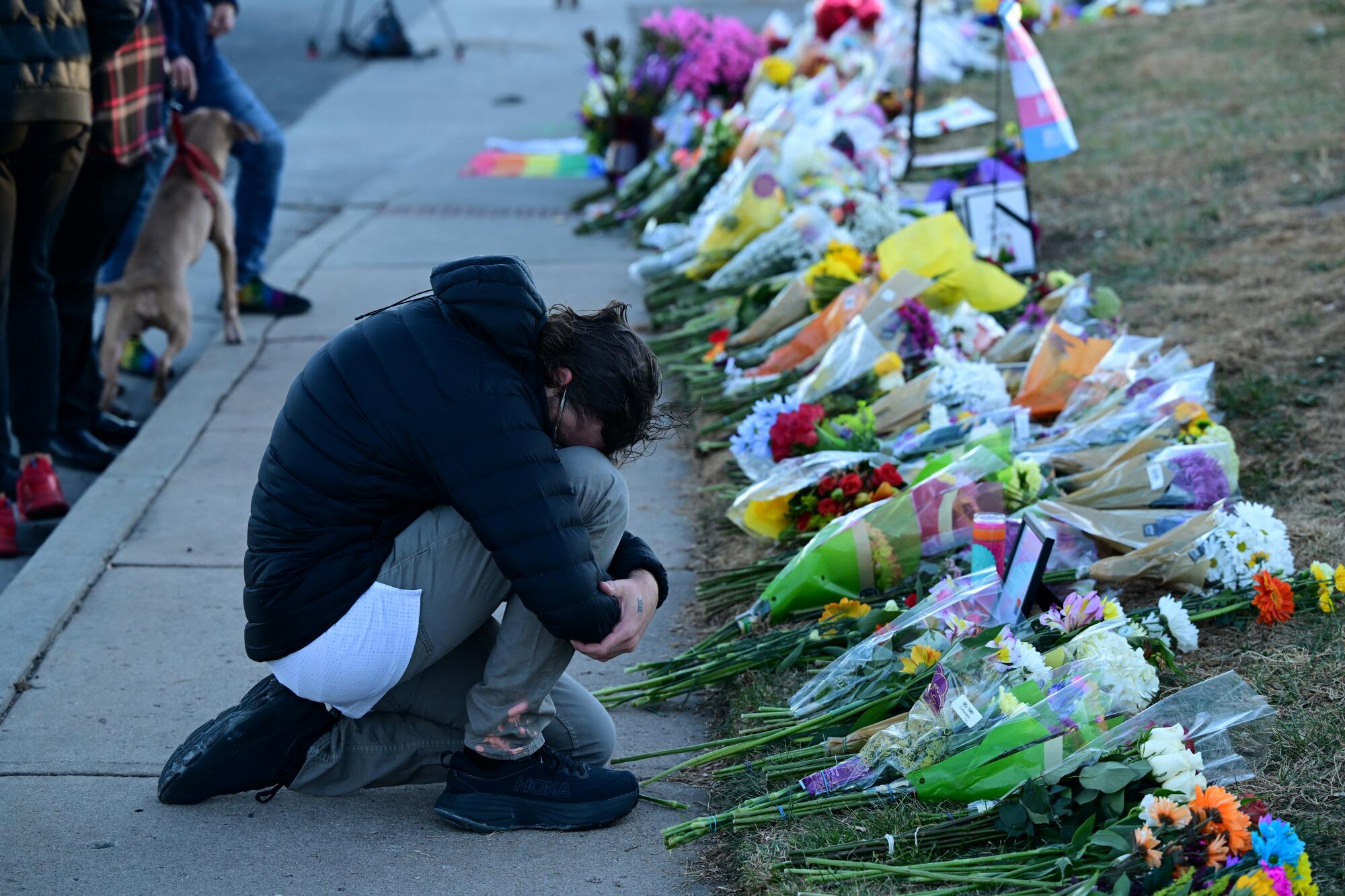 A man places his head on his knees as he pays his respects at a makeshift memorial near Club Q.