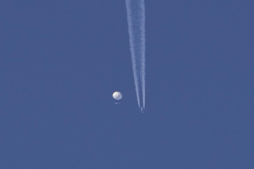 A large balloon drifts above the Kingston, N.C. area, with an airplane and its contrail seen below it.  