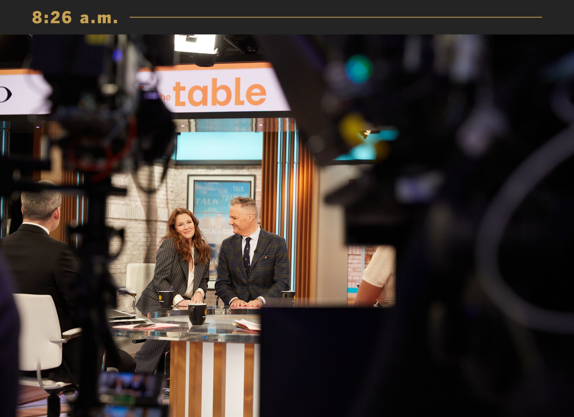 Drew Barrymore sits next to a man on the set of a talk show.