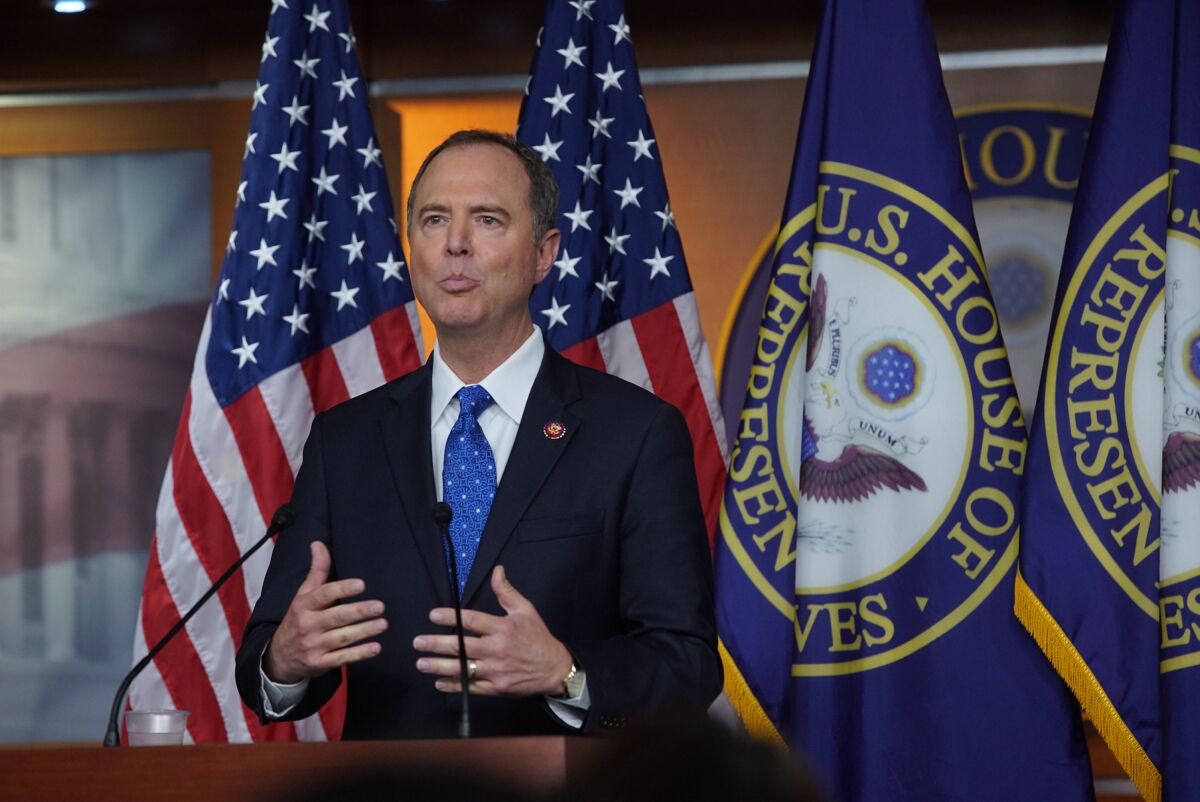 Adam Schiff speaks at a lectern in front of a row of flags. 