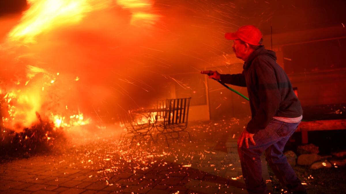 A resident tries to battle a shrub fire as the Thomas fire burns in the town of La Conchita early Thursday morning.