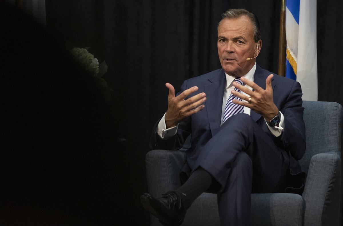 L.A. mayoral candidate Rick Caruso gestures with his hands while he sits in a chair and speaks.