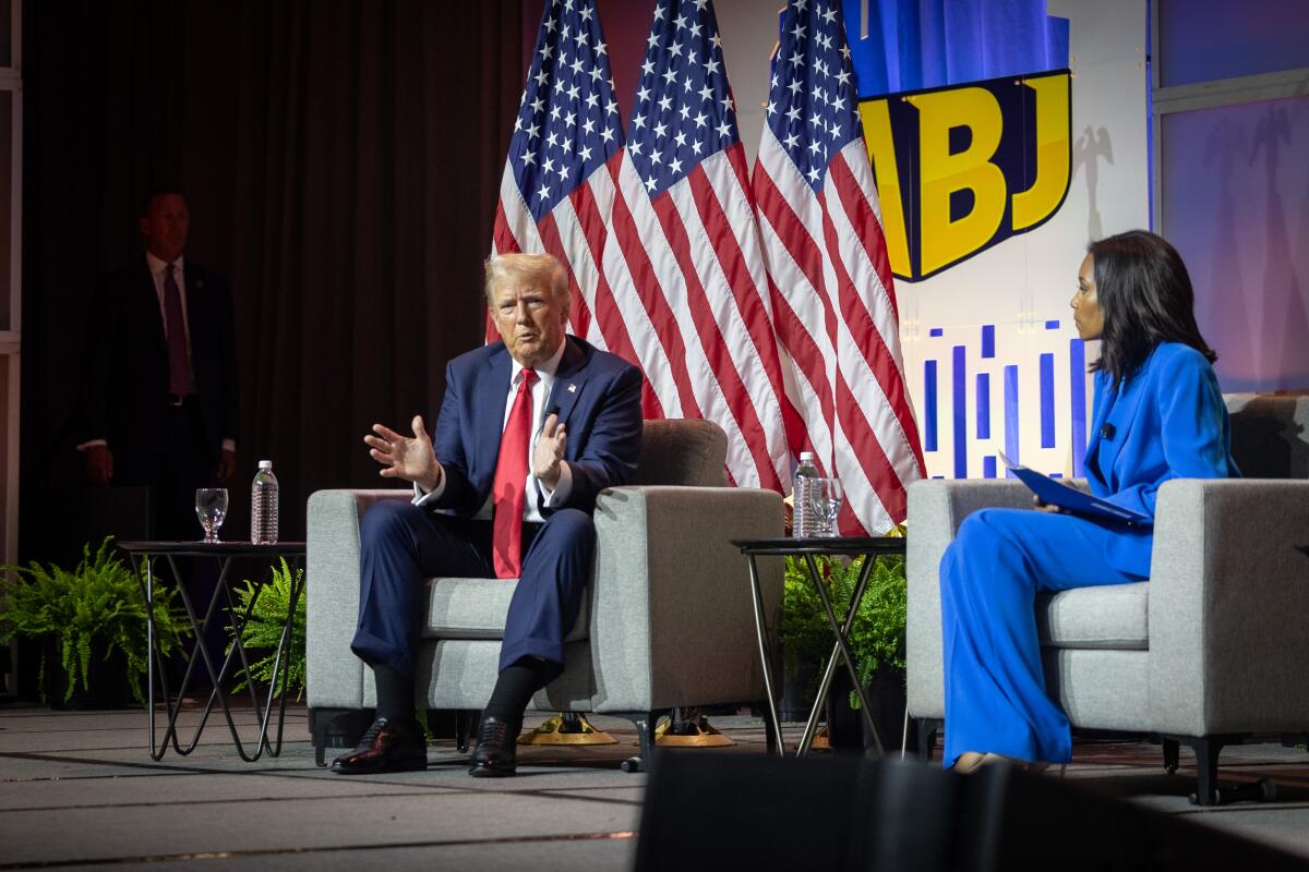 Donald Trump on stage with a woman, both sitting in chairs.