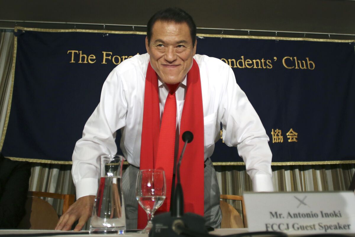 Antonio Inoki, wearing a red scarf, bows at a news conference