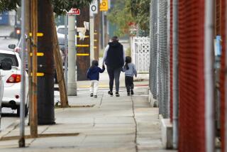 Wilmington, Los Angeles, California-Dec. 7, 2021-A woman walks with two young children along the playground at Wilmington Park Elementary on Dec. 7, 2021, where a 9-year-old girl was hit by a stray bullet yesterday afternoon, Dec. 6, 2021. A 13-year-old boy was killed and two other people were injured, including a 9-year-old girl, in a shooting in Wilmington late Monday afternoon. A 9-year-old girl playing nearby at Wilmington Park Elementary School was hit by a stray bullet, prompting a separate 911 call. She was hospitalized in critical condition. (Carolyn Cole / Los Angeles Times)