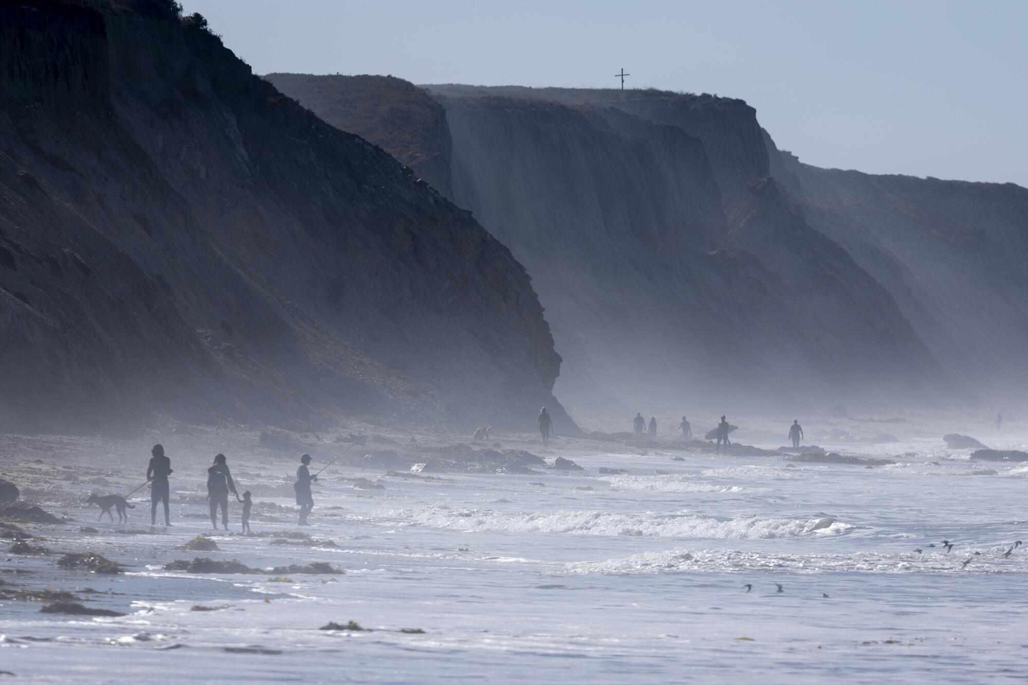 Beachgoers walk along the surf at the base of tall bluffs.