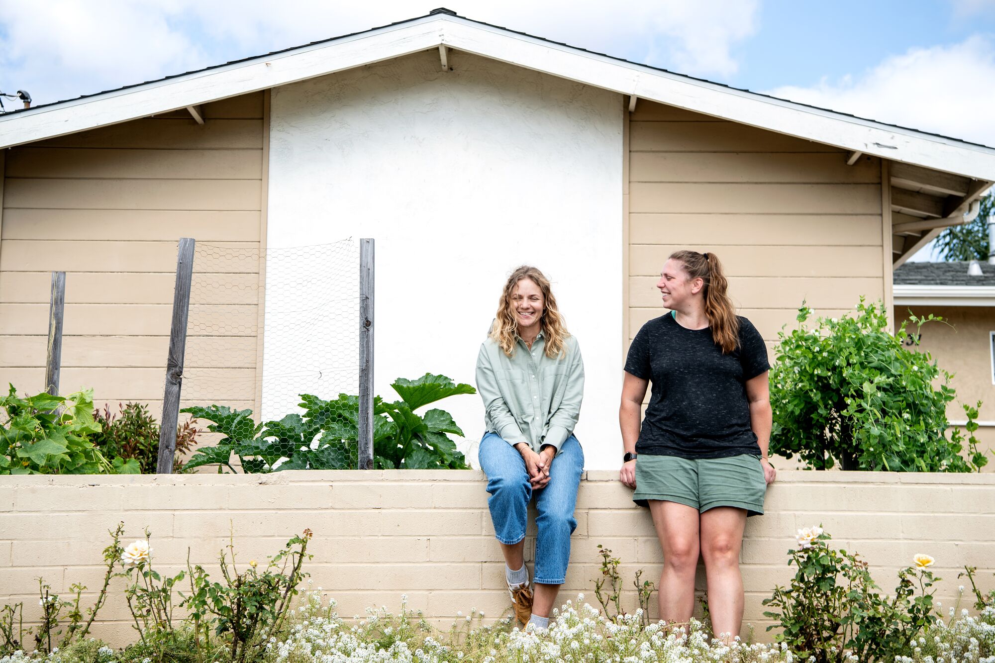 Rachel Nafis and Kristen Kellogg stand in a garden outside a house.