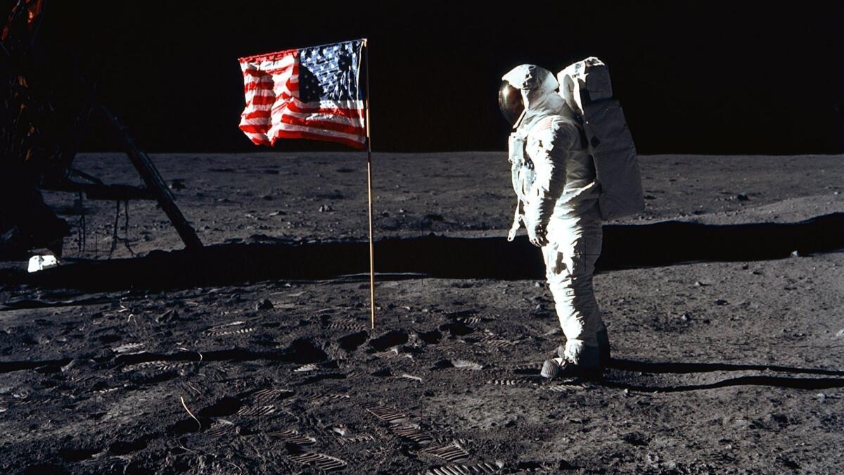 AS11-40-5874 (20 July 1969) --- Astronaut Edwin E. Aldrin Jr., lunar module pilot of the first lunar landing mission, poses for a photograph beside the deployed United States flag during Apollo 11 extravehicular activity (EVA) on the lunar surface. The Lunar Module (LM) is on the left, and the footprints of the astronauts are clearly visible in the soil of the moon. Astronaut Neil A. Armstrong, commander, took this picture with a 70mm Hasselblad lunar surface camera. While astronauts Armstrong and Aldrin descended in the LM the "Eagle" to explore the Sea of Tranquility region of the moon, astronaut Michael Collins, command module pilot, remained with the Command and Service Modules (CSM) "Columbia" in lunar orbit.