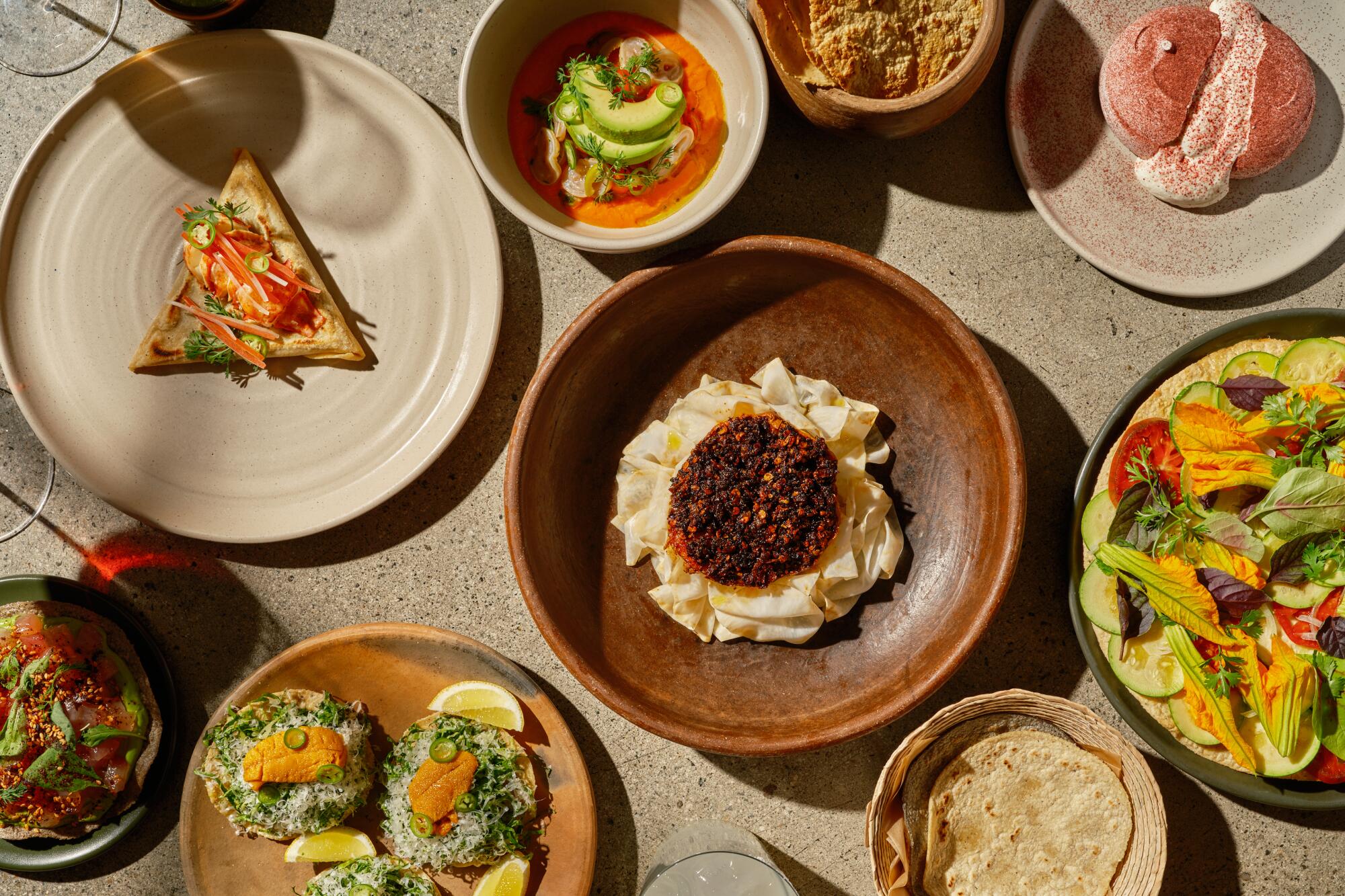 An overhead view of an array of dishes from Damian on a concrete surface.