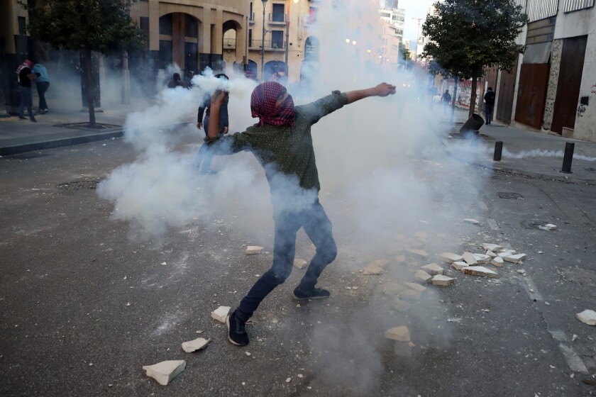 A protester throws back a tear gas canister towards riot policemen, during a protest near Parliament Square, In Beirut, Lebanon, Saturday, March. 13, 2021. Riot police fired tear gas to disperse scores of people who protested near parliament building in central Beirut Saturday amid deteriorating economic and financial conditions and as the local currency hit new low levels. (AP Photo/Bilal Hussein)