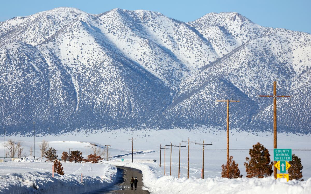 People walk along a snow-lined road toward a mountain range in California
