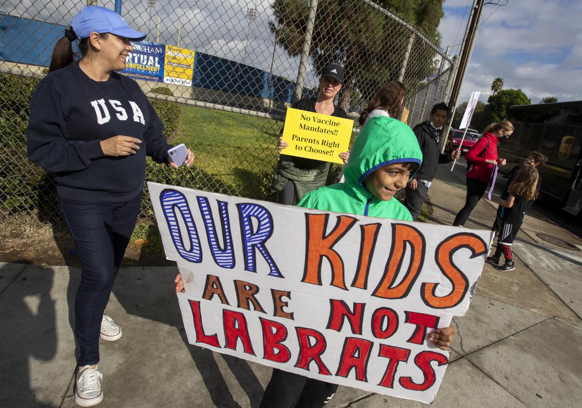 Adults and kids hold signs at a street corner against COVID vaccine mandates.