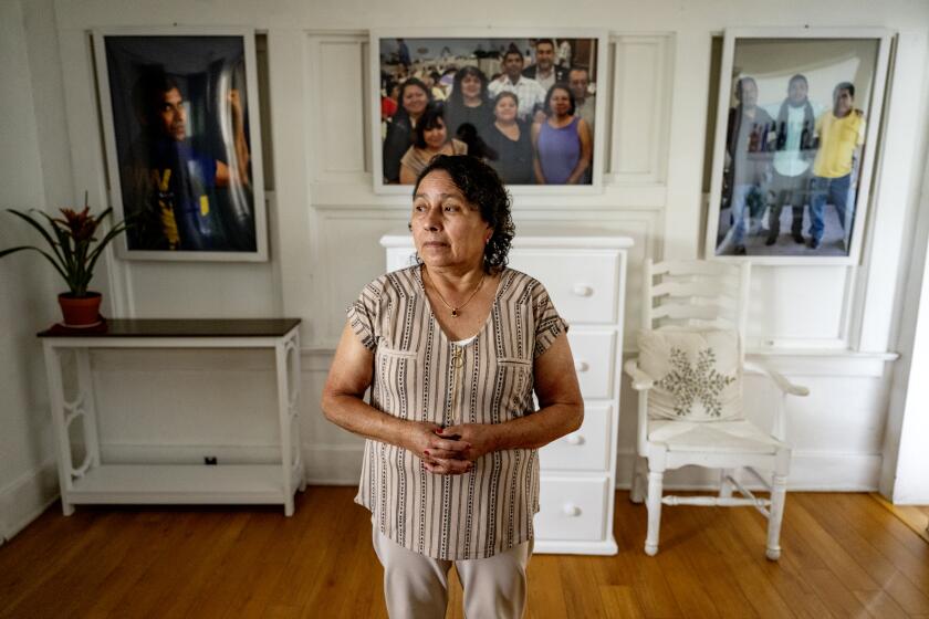 LOS ANGELES, CA -APRIL 17, 2023: Dora Molina stands in front of large family photos including of her late husband Jose Tomas Mejia who was stabbed to death by a juvenile where he worked at Park La Brea two years ago on April 17, 2023 in Los Angeles, California. The juvenile, now18, was sentenced Monday to a secure youth treatment facility until her turns 25. The juvenile was trying to steal Mejia's keys when the stabbing occurred.(Gina Ferazzi / Los Angeles Times)