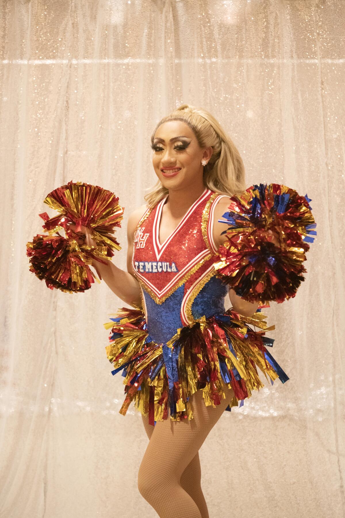 Andrei Manila holding pom-poms in a red, blue and gold cheerleader outfit