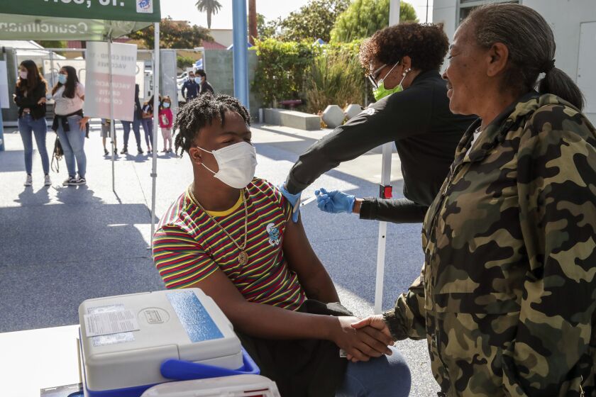 Los Angeles, CA - June 24: Kalvin Green,15, left, holds the hand of his mother Marilyn Green as nurse Marie Eddins administers COVID19 vaccine at mobile clinic held at Los Angeles City Councilman Curren Price's district office. First 50 recipient of the vaccine got a free pair of ``Beats by Dre'' headphones. Councilman Curren Price's district office on Thursday, June 24, 2021 in Los Angeles, CA. (Irfan Khan / Los Angeles Times)