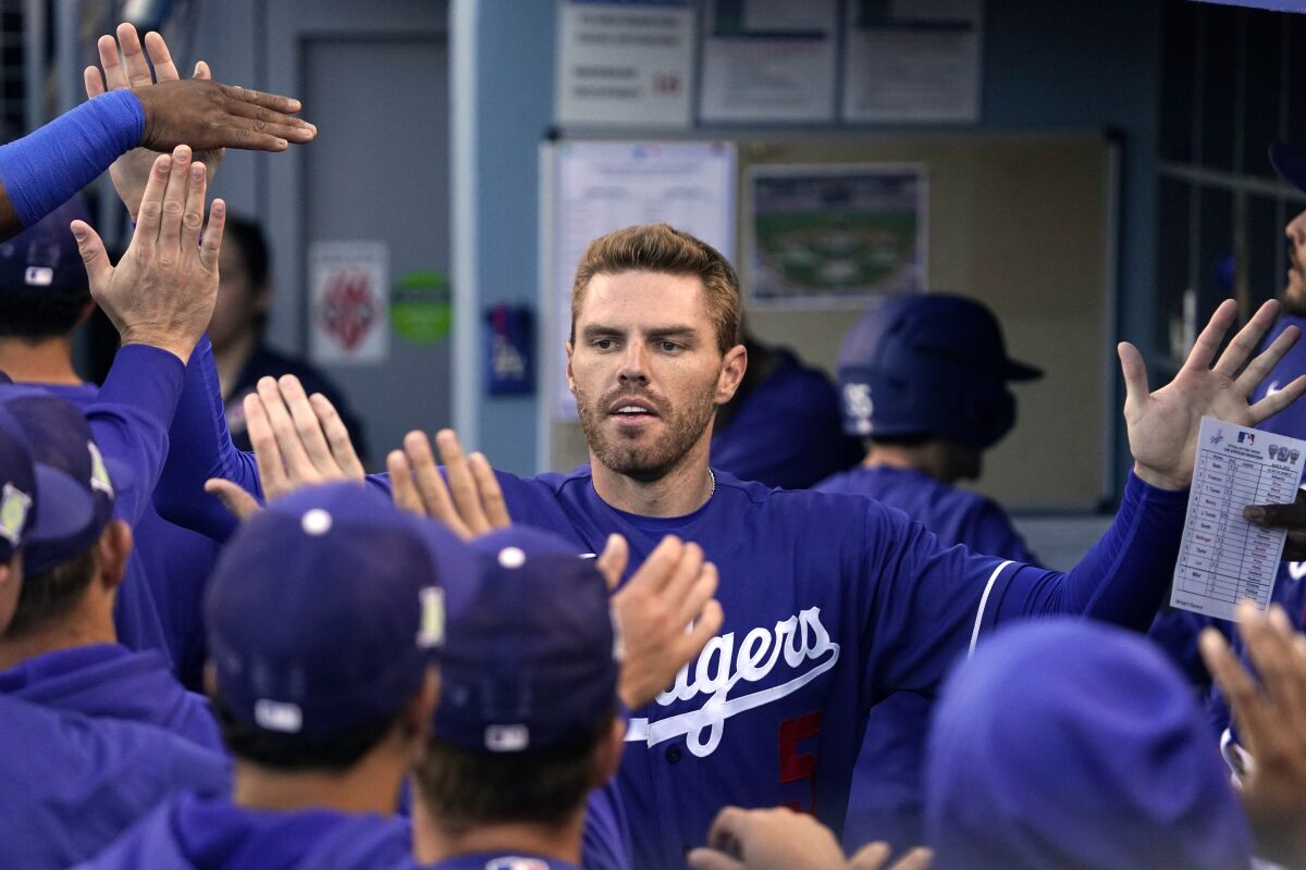 Los Angeles Dodgers' Freddie Freeman is congratulated by teammates in the dugout after scoring on a double by Trea Turner during the first inning of a spring training baseball game against the Los Angeles Angels Tuesday, April 5, 2022, in Los Angeles. (AP Photo/Mark J. Terrill)