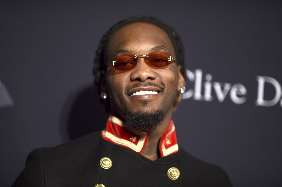 A man with braids and sunglasses in a black jacket smiling