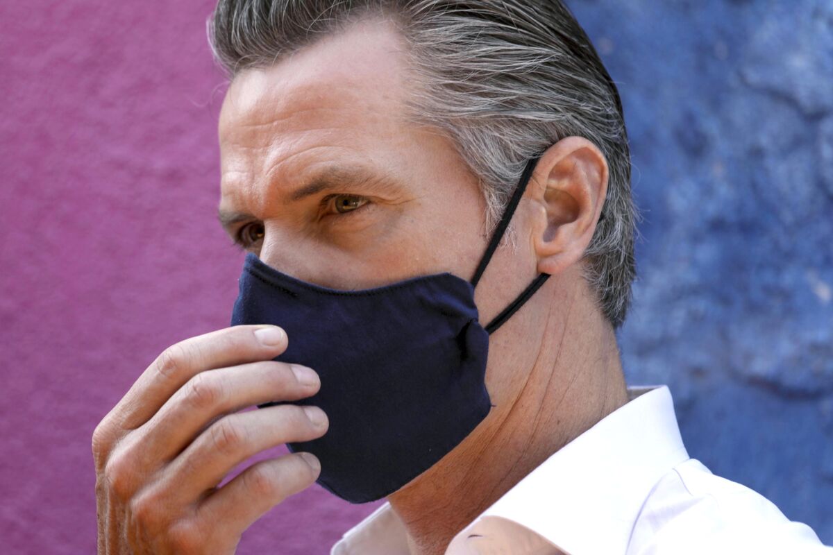 California Gov. Gavin Newsom with a mask on in front of a pink and blue wall