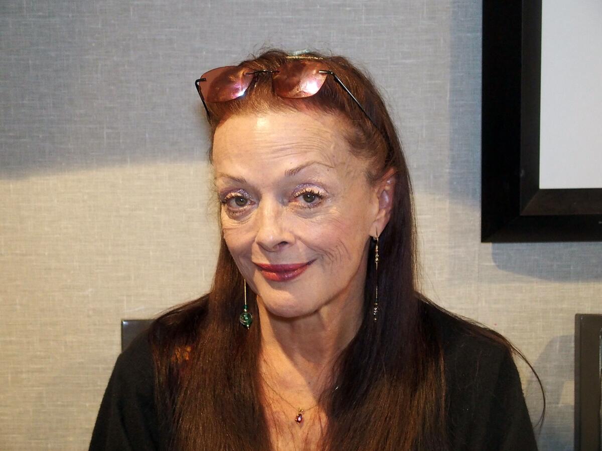A woman with long red hair and sunglasses on her head wearing a black shirt and red lipstick