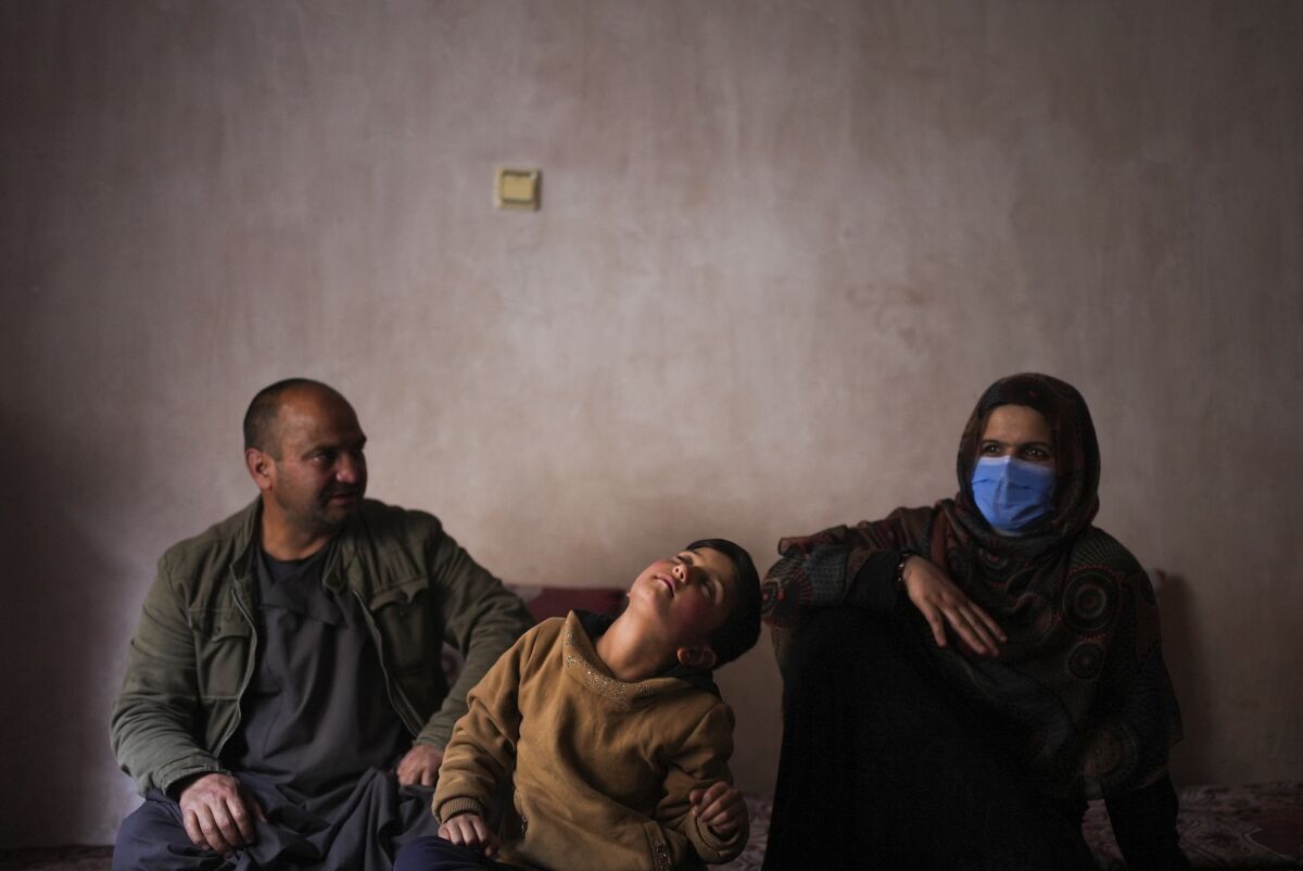 An Afghan child with short hair sits between her parents.