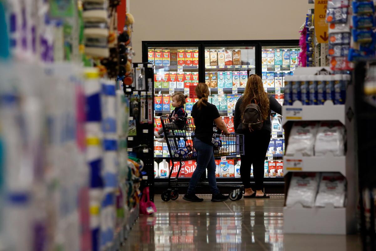 A baby sits in a cart as two women stop in front of the dairy case at a Smart & Final.