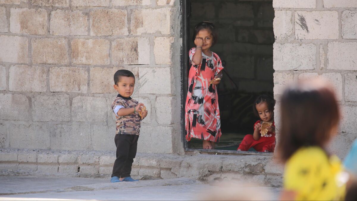 Syrian children stand in front of a house in the Kurdish-majority northeastern city of Qamishli.