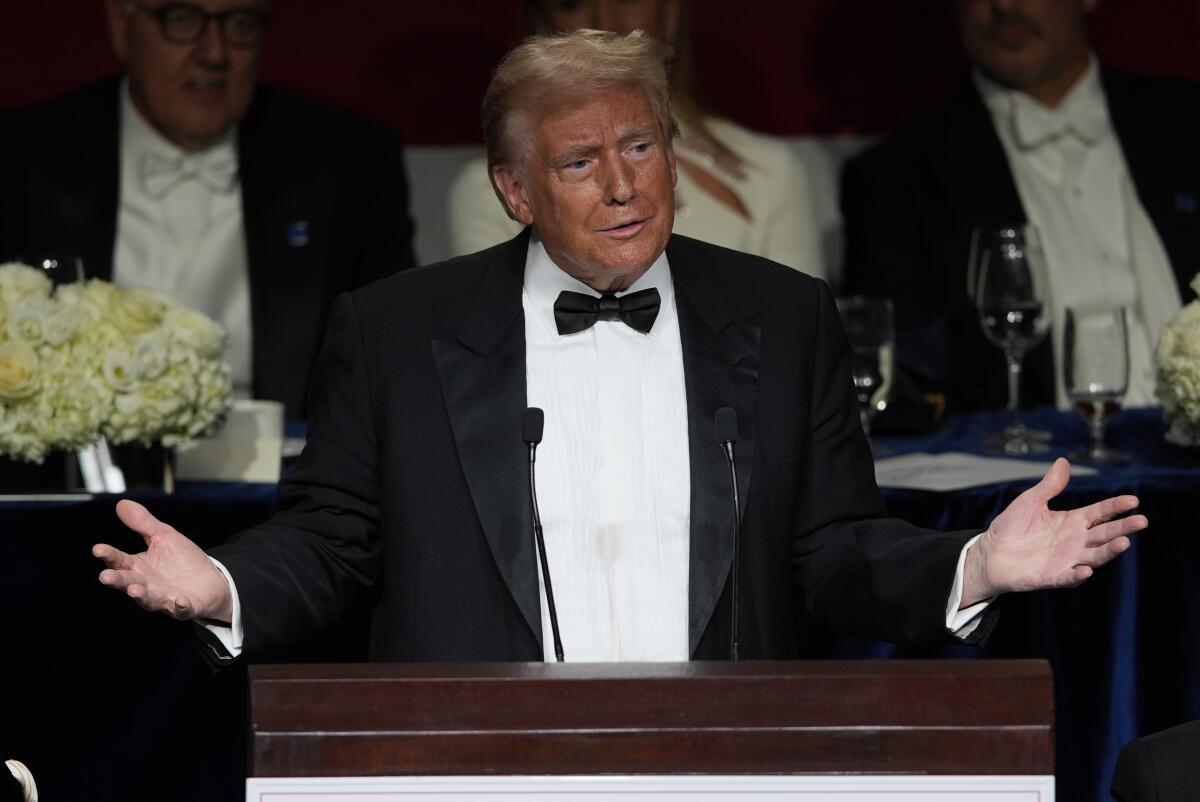 A man in a tuxedo gesturing and speaking at a podium 