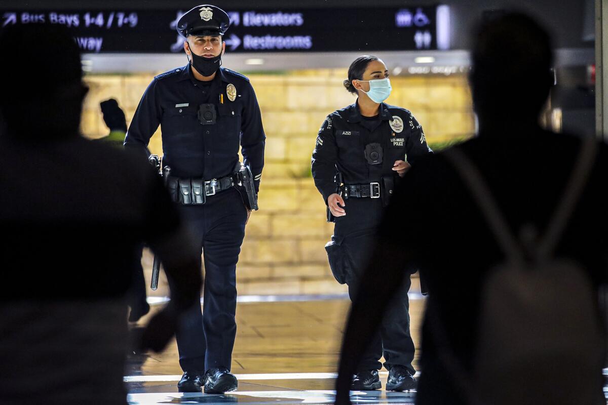 Two police officers, one wearing a mask and the other with it below his mouth, patrol Union Station