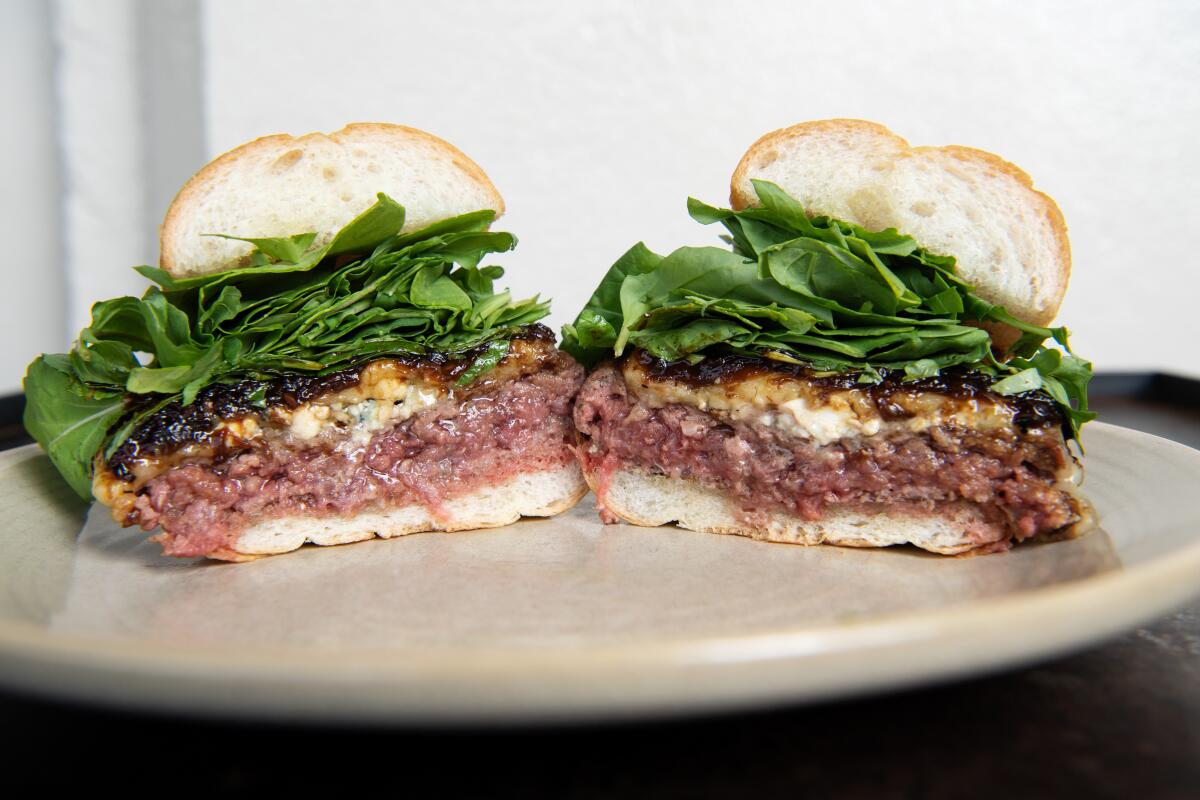 Two halves of a burger on a white bun, arranged on a plate to show juicy pink patties and melted toppings stacked with greens